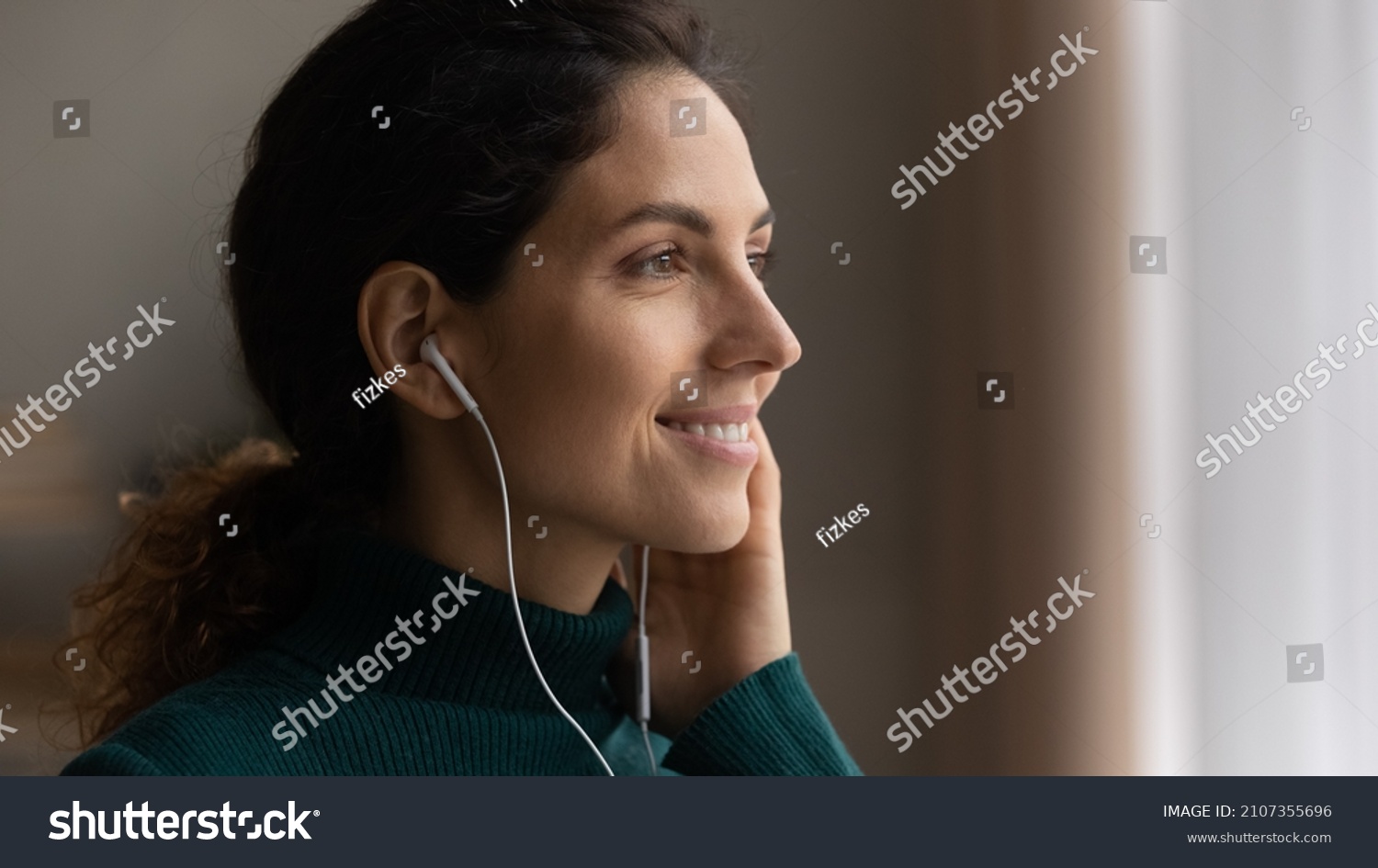 Close up head shot young attractive woman listening favorite popular music in wired earphones, looking in distance, daydreaming or enjoying peaceful calm weekend pastime alone at home, hobby activity. #2107355696