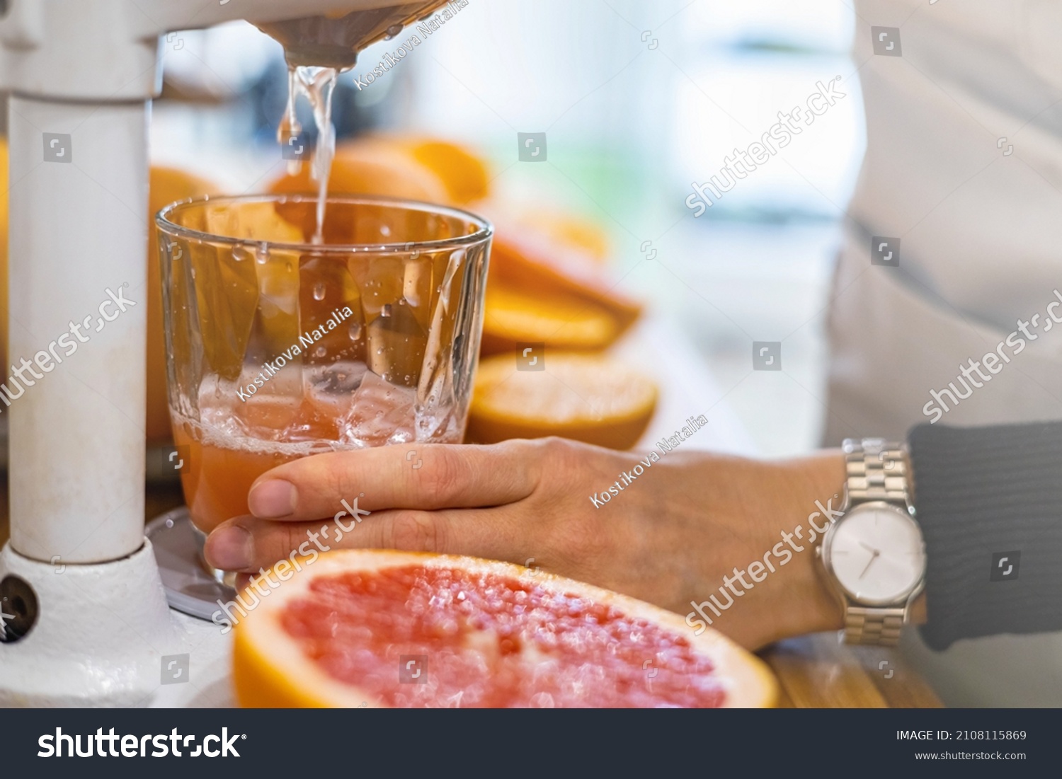 Closeup female bartender hands makes fresh detox grapefruit juice pulling handle professional citrus and pomegranate press. Woman kitchen staff cooking fruits refreshing vitamin drink in lever juicer #2108115869