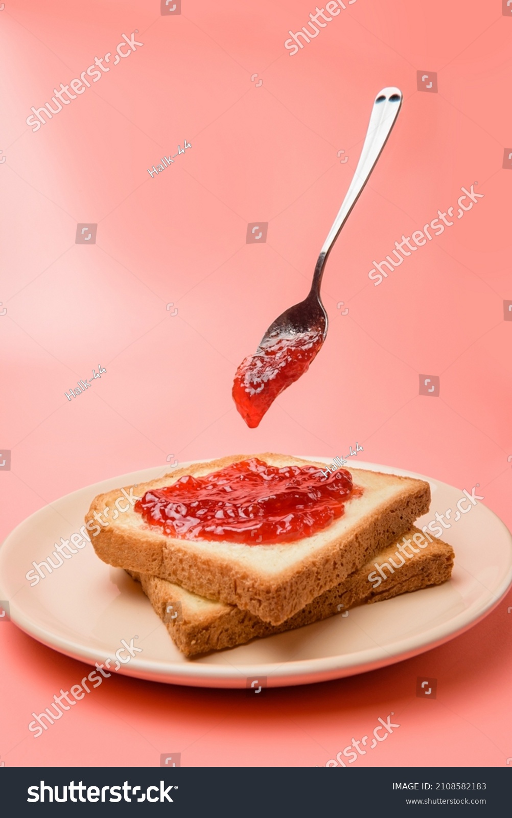 a dish of toast spread with jam and a levitating spoon against a pastel pink background. #2108582183