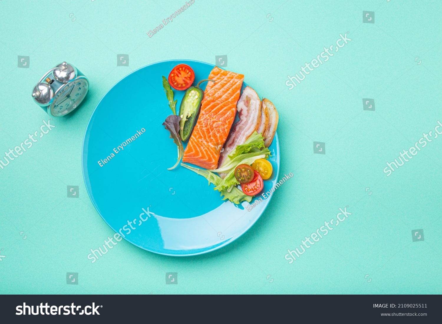 Intermittent fasting low carb hight fats diet concept flat lay, healthy food salmon fish, bacon meat, vegetables and salad on blue plate and clock alarm on blue background top view, space for text #2109025511