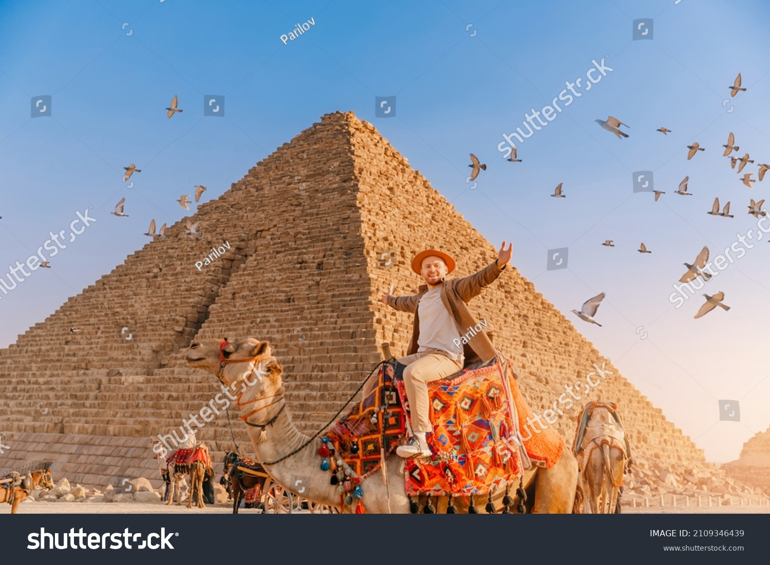 Tourist man with hat riding on camel background pyramid of Egyptian Giza, sunset Cairo, Egypt. #2109346439
