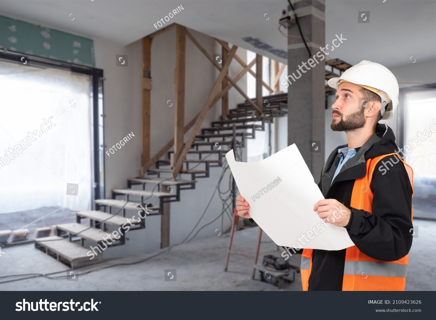 An architect with drawings in his hands. Man supervises construction work. Foreman in house under construction. A construction engineer in a hard hat and an orange vest. Builder with drawings. #2109423626