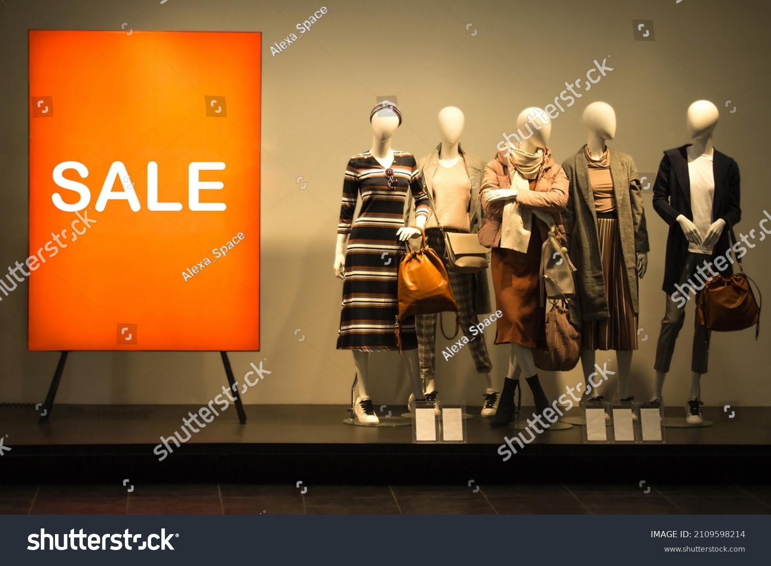 Female mannequins near red stand ''Sale''. Standing dummies in spring autumn collection. Shop window clearance #2109598214