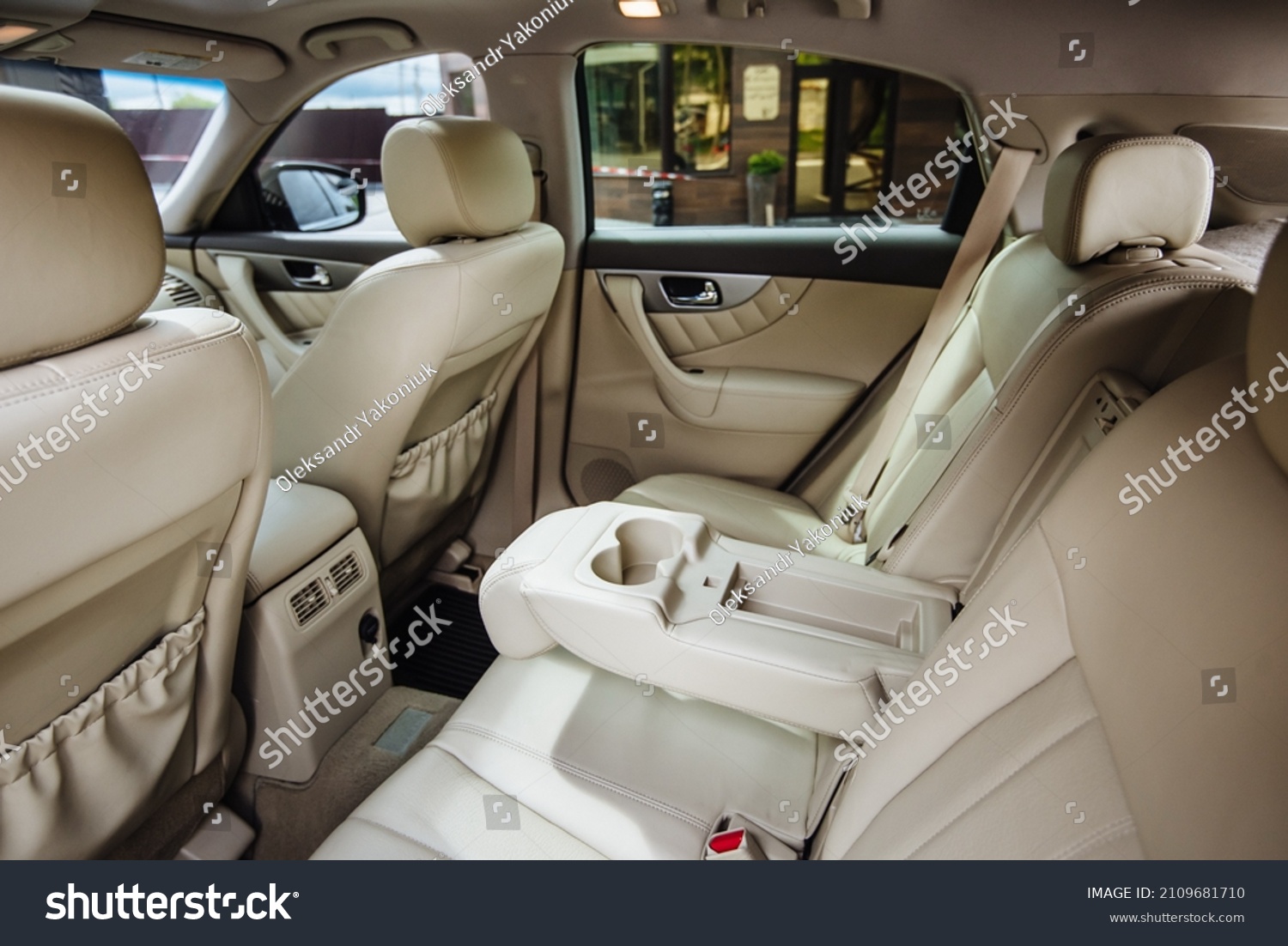 Luxury car interior made of white leather. Leather folding armrest armrest with cup holders in rear seats inside a vehicle. Clean leather interior: white rear seats, headrests and belts. #2109681710