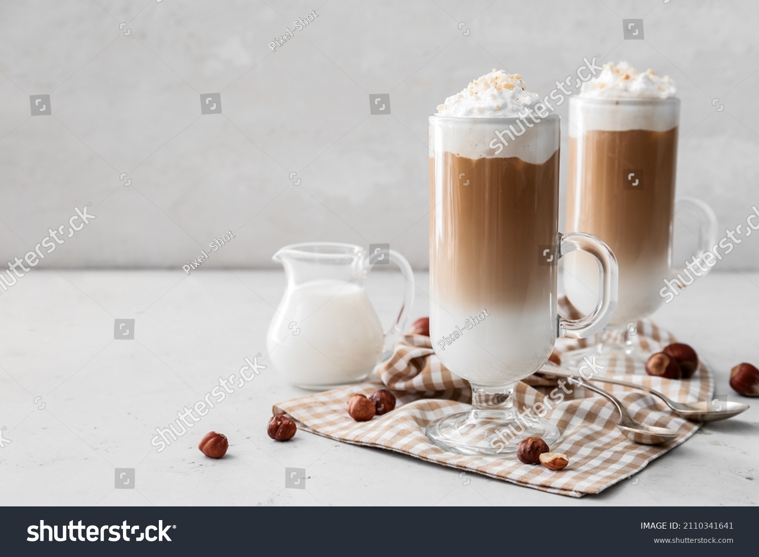 Glass cups of tasty latte and jug with milk on white background #2110341641