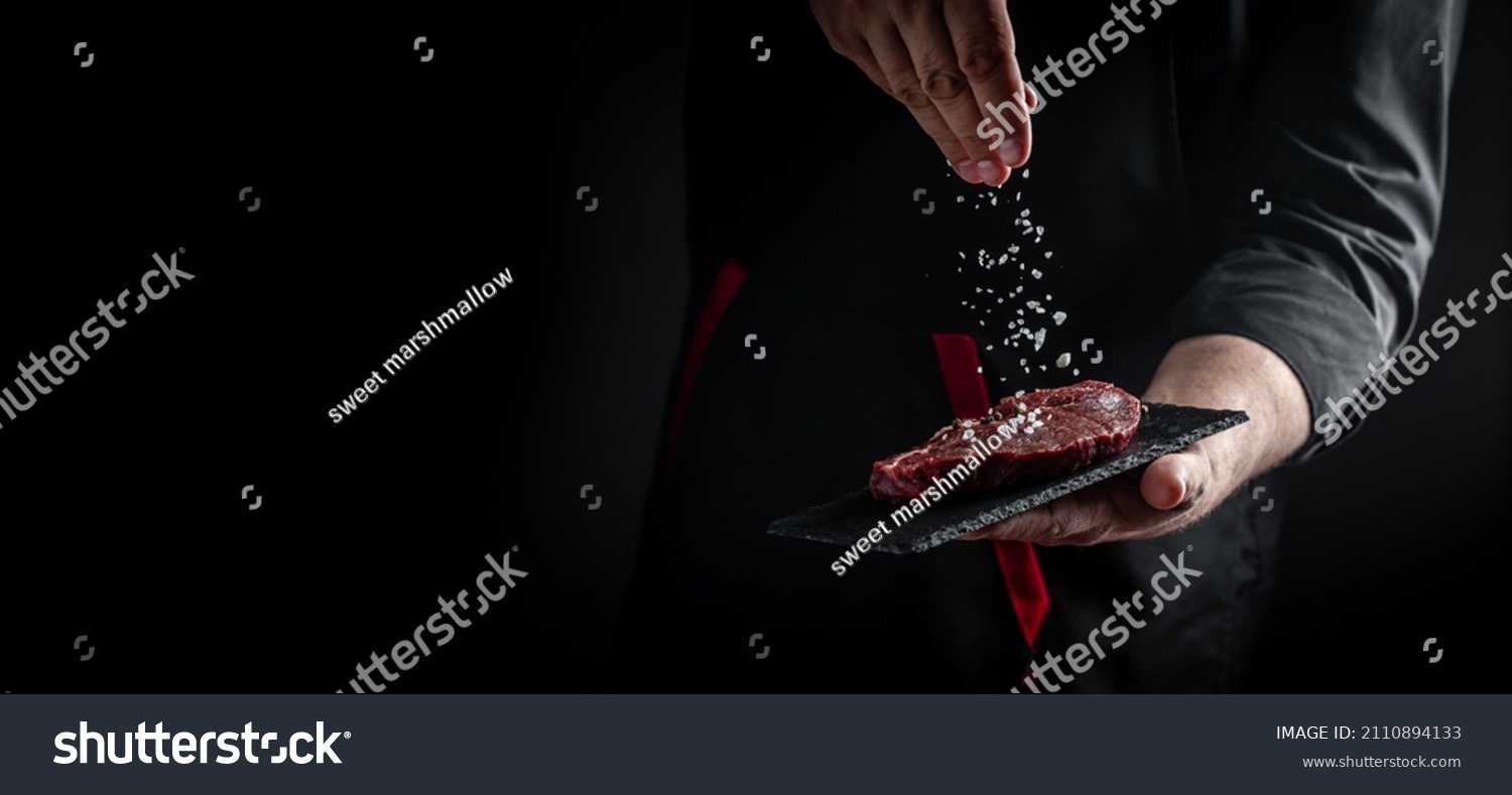 Chef hands cooking meat steak and adding seasoning in a freeze motion. Fresh raw Prime Black Angus beef rump steak. banner, menu recipe. #2110894133