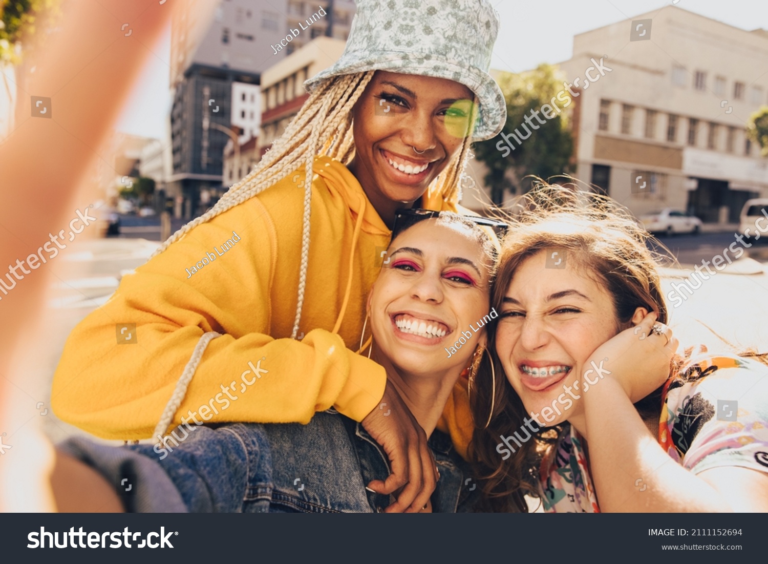 Trio of friends taking a selfie together. Group of multiethnic female friends having fun together outdoors. Cheerful generation z friends capturing their happy moments in the city. #2111152694