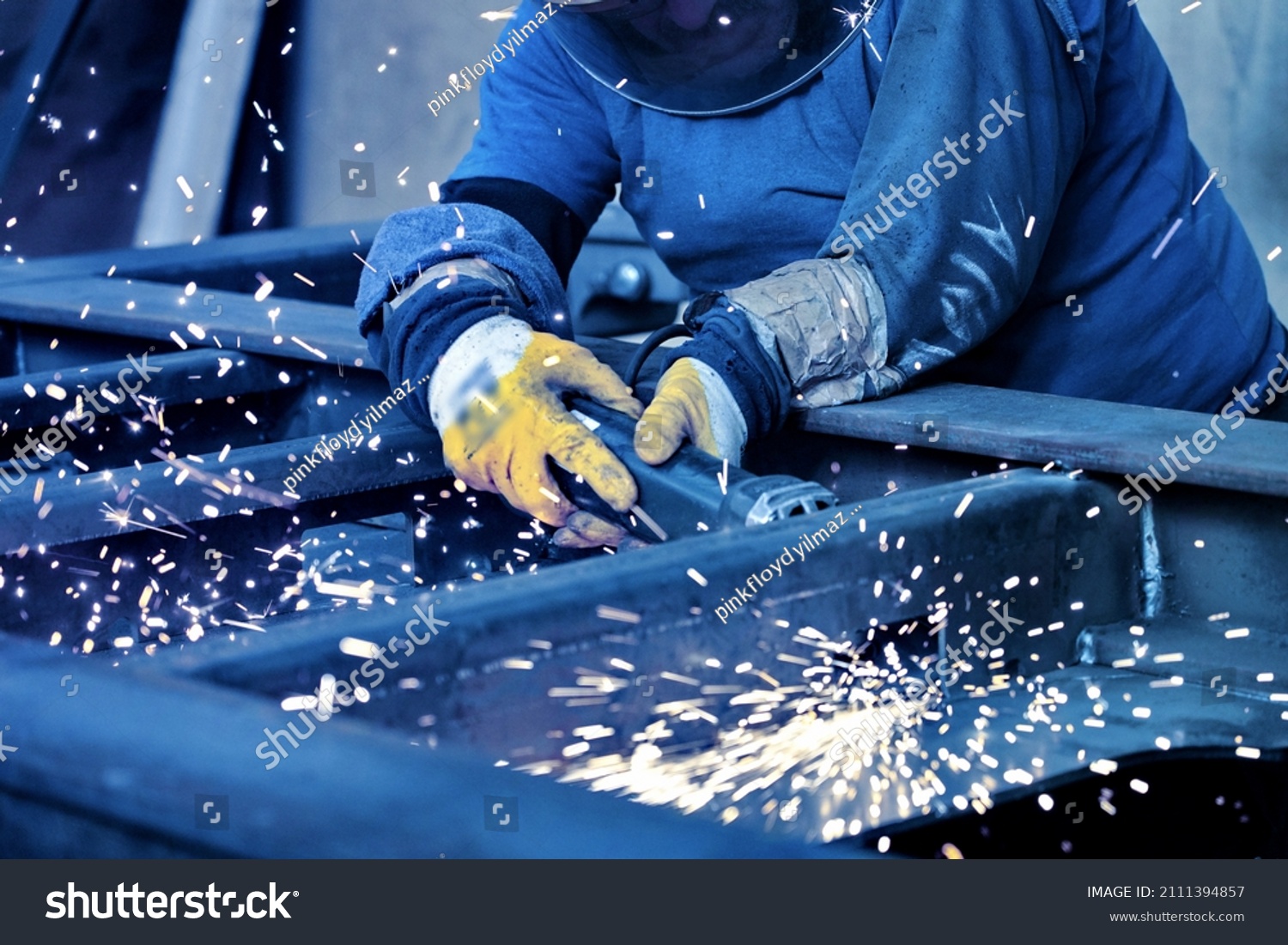 A welder welds metal into his workshop. Blue welding sparks. Gas combustion and blue smoke. Small welding workshop. Welding juncture of metal construction #2111394857