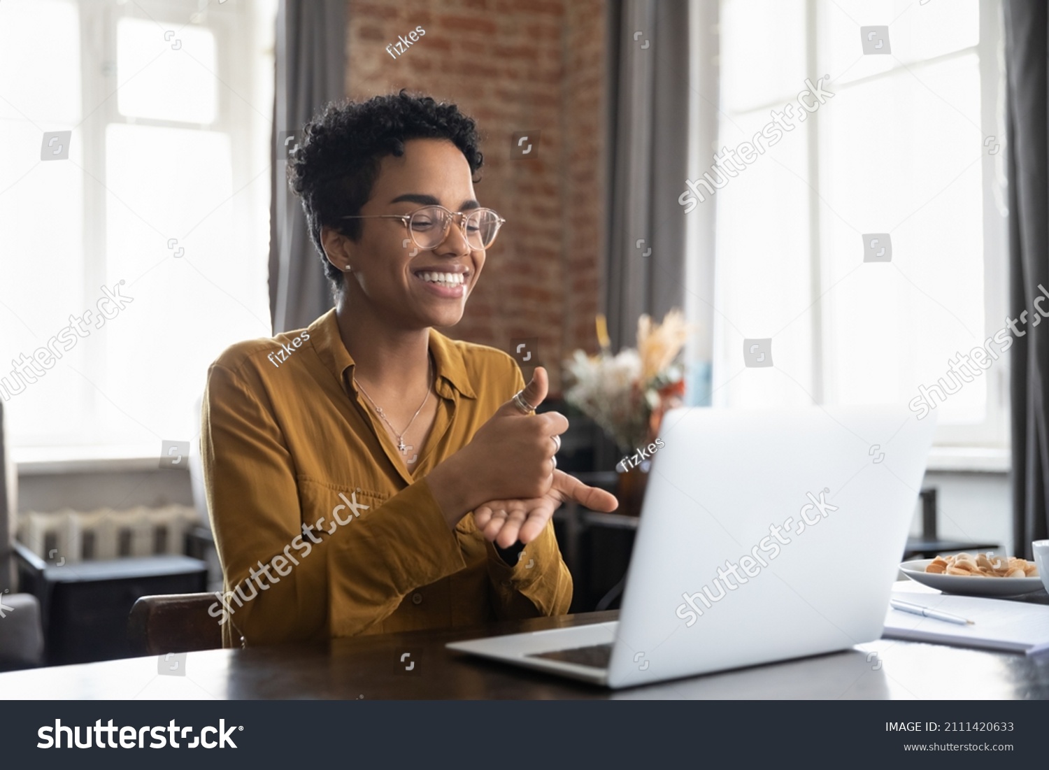 Smiling friendly African American therapist in glasses talking on video call, using sign language, speaking to patient with hearing disability, deafness, showing gestures at screen #2111420633