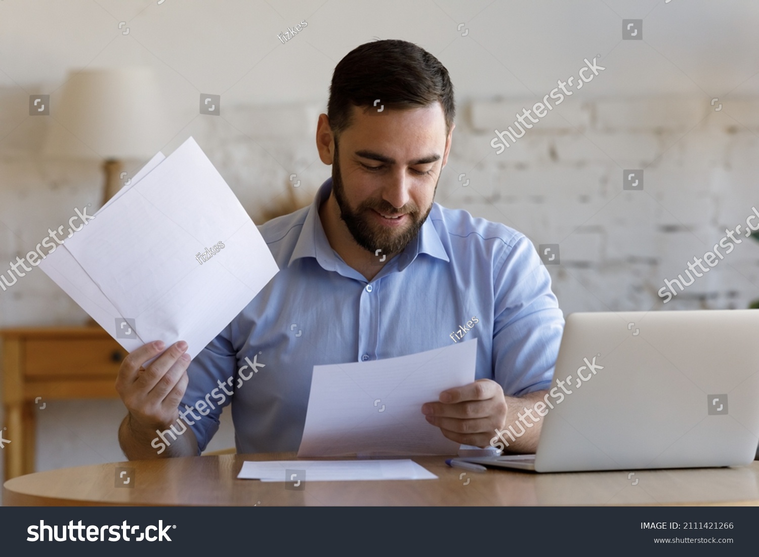 Satisfied smiling business man doing paperwork at home workplace. Entrepreneur reading financial reports, reading documents. Tenant making payment for rent, reviewing bills, bank mortgage notice #2111421266