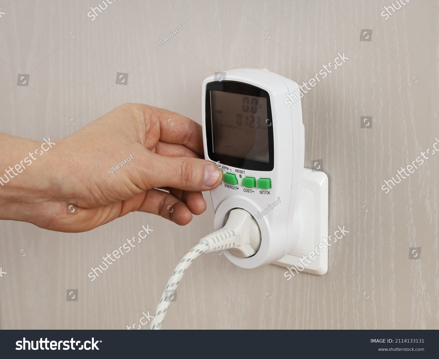 Hand presses button in wattmeter on wall, for measuring electricity costs in device, close-up #2114133131