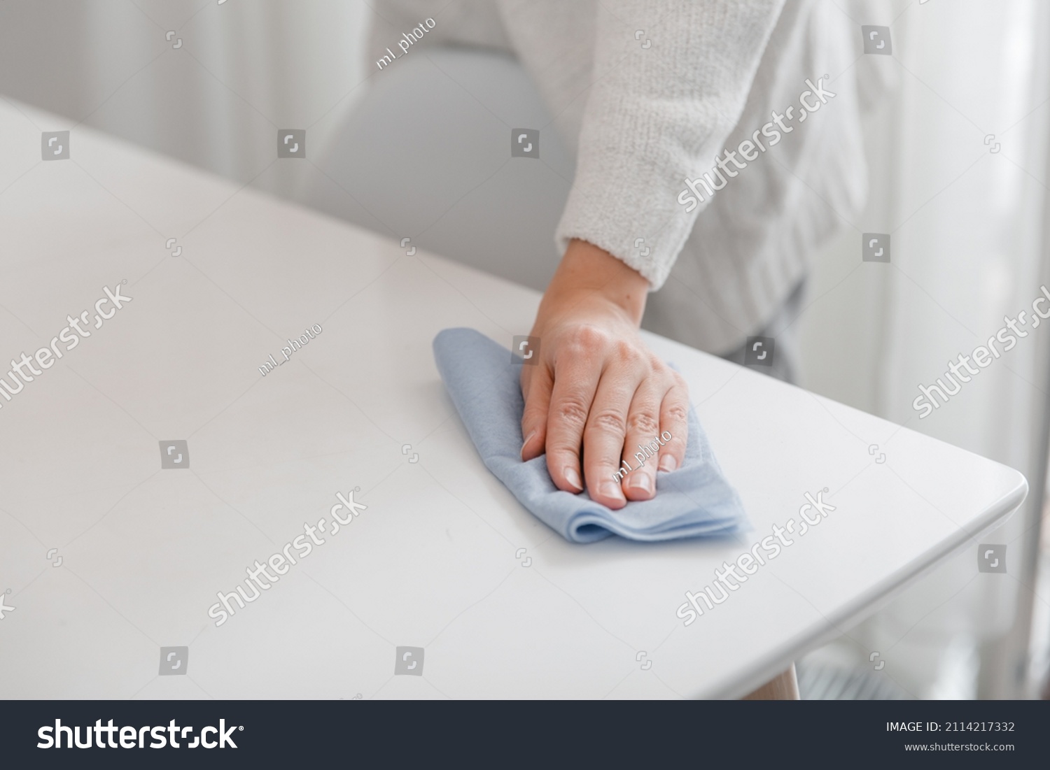 Cleaning the table with a blue microfiber cloth. Sanitize surfaces prevention in hospital and public spaces against coronavirus. Woman hand using wet wipe at home. Cleaning the room. #2114217332
