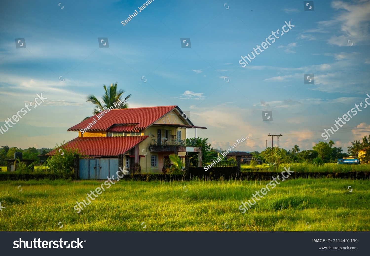 Traditional Indian village house surrounded by green grass and beatiful cloudy blue sky. Village landscape. #2114401199