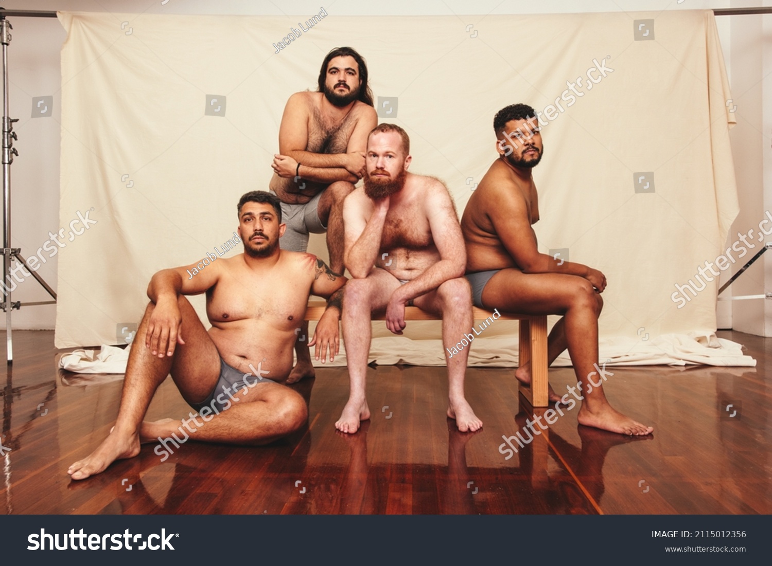 Shirtless and confident. Four body positive men looking at the camera while wearing underwear in a studio. Group of self-assured men embracing their natural bodies together. #2115012356
