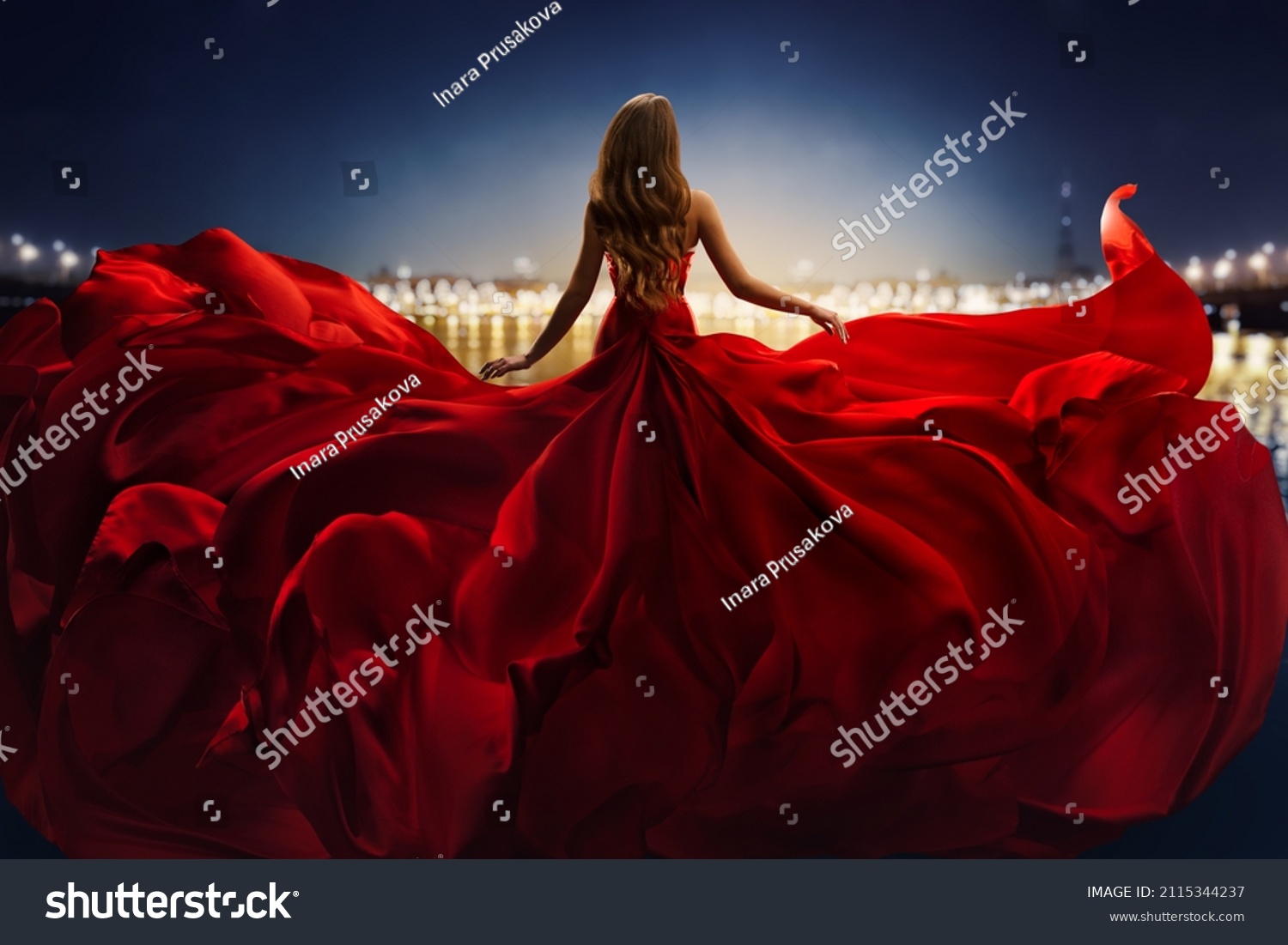 Fashion Woman in Red fluttering Dress Back Side Rear View. Glamour Model dancing with Long Silk Fabric flying on Wind over Night Sky City Light Landscape #2115344237