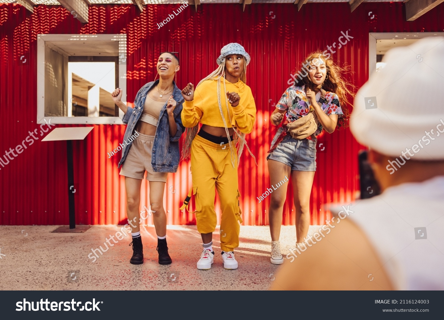 Following fun social media trends. Group of generation z friends doing trendy dance moves in front of a camera phone. Vibrant young people creating content for their social media vlog. #2116124003