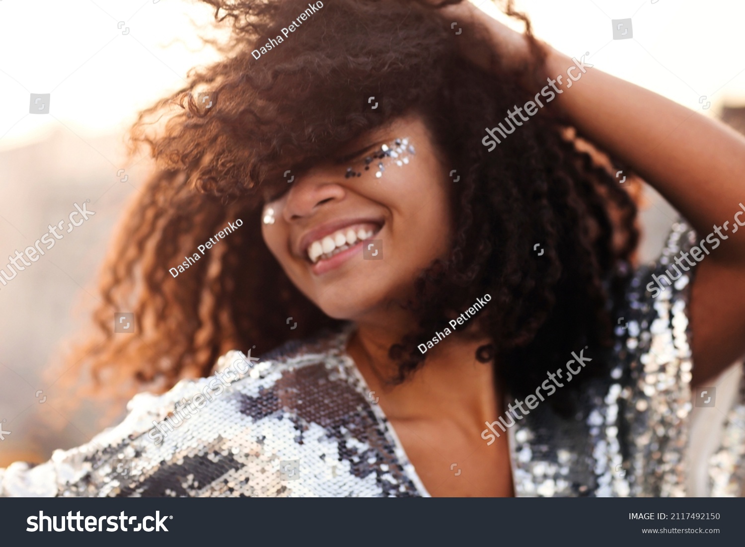 Portrait of overjoyed glamour african american woman with glitter on face in silver sequin dress enjoying outdoor party or event, mixed race female in festive wear with eyes closed feeling happy #2117492150