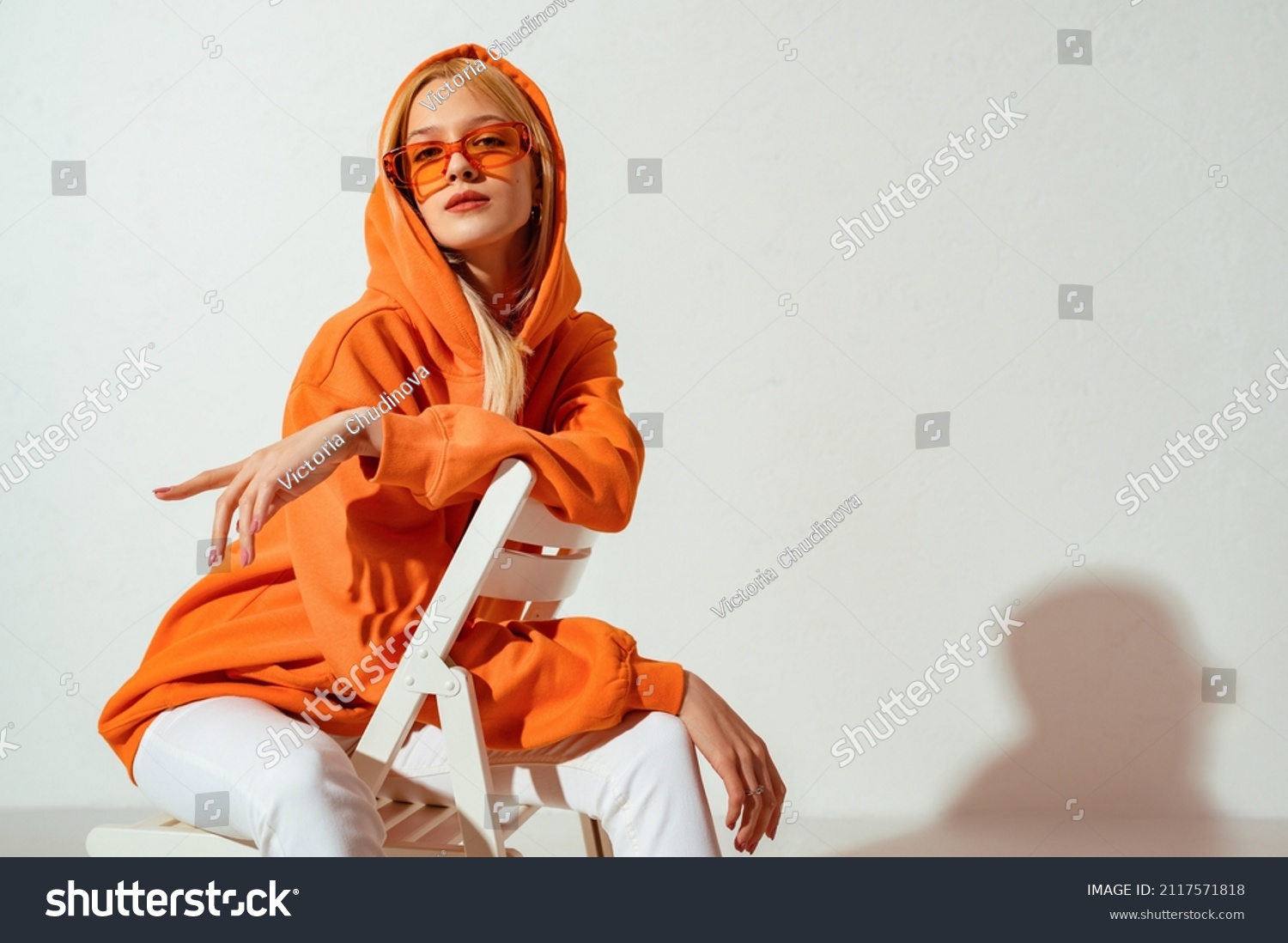 Fashionable confident blonde woman wearing trendy orange sweatshirt, color sunglasses, posing on white background. Copy, empty space for text #2117571818