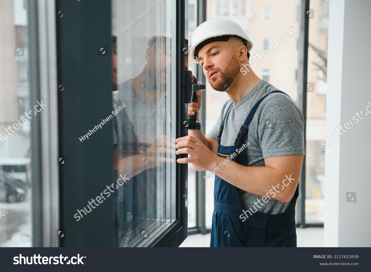 Workman in overalls installing or adjusting plastic windows in the living room at home #2117622839