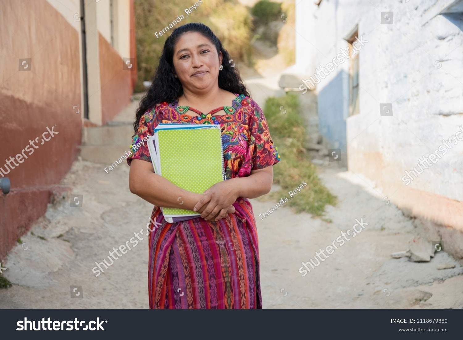 Hispanic mom with notebooks outside school in rural area - Mayan adult woman ready to go to study - Latina teacher in town #2118679880