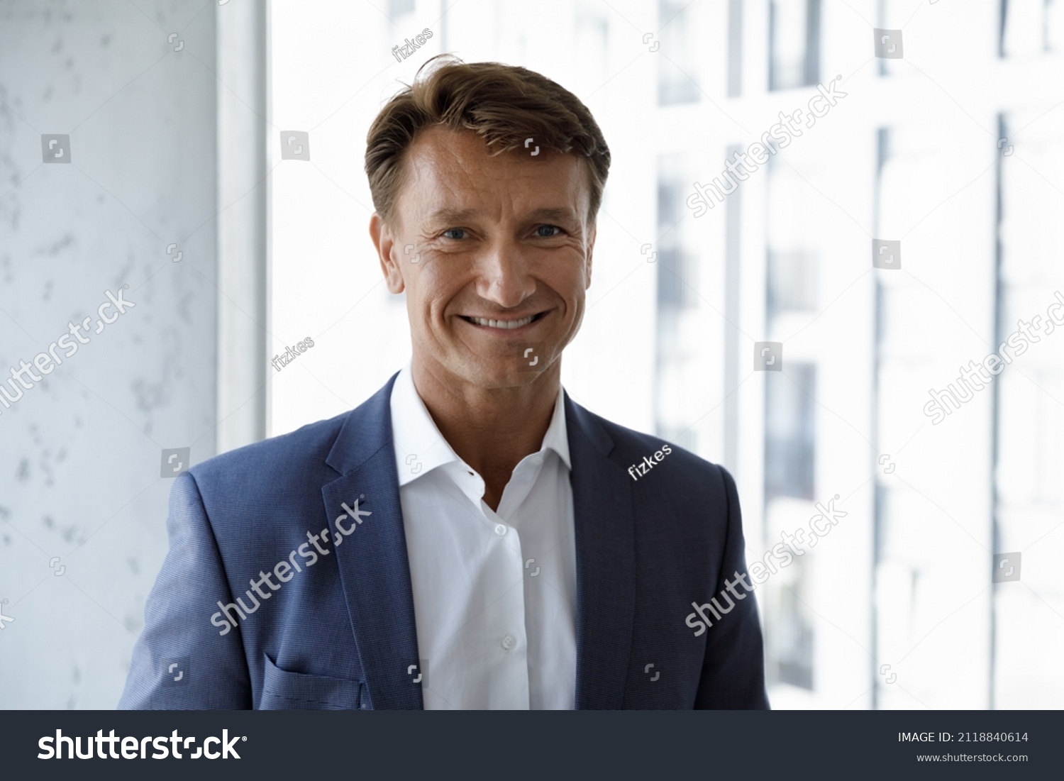 Happy mature male business leader head shot portrait. Confident middle aged 50s businessman, CEO, executive in formal suit looking at camera, smiling, standing at office window. Job success concept #2118840614
