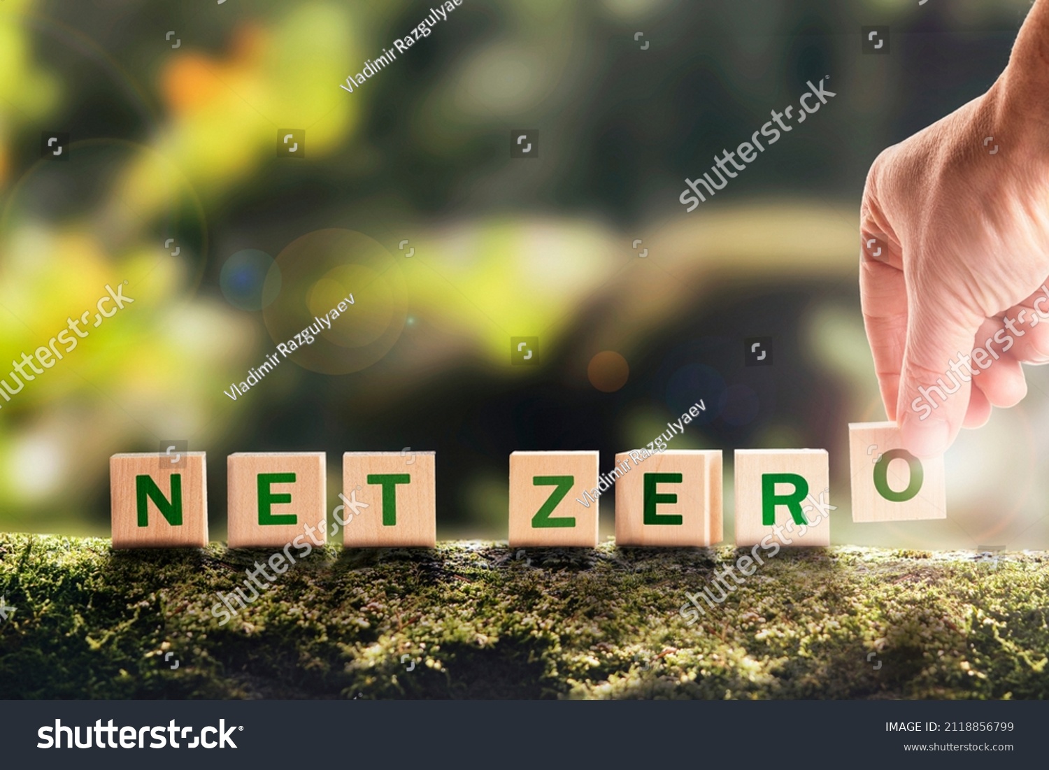 Net zero 2050 Carbon neutral. Net zero greenhouse gas emissions target. Climate neutral long strategy. No toxic gases. Hand puts wooden cubes with netzero icon in green background copy space. #2118856799