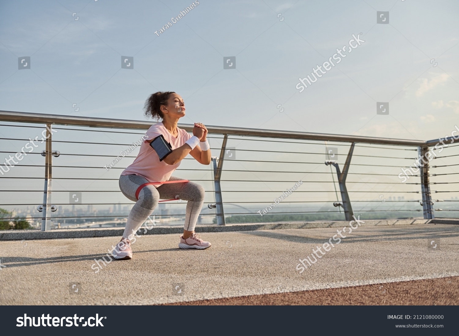 Determined middle aged sportswoman, female athlete exercising outdoor at sunrise, doing squats with elastic resistance band. Fitness sport endurance, body weight training and active lifestyle concept #2121080000