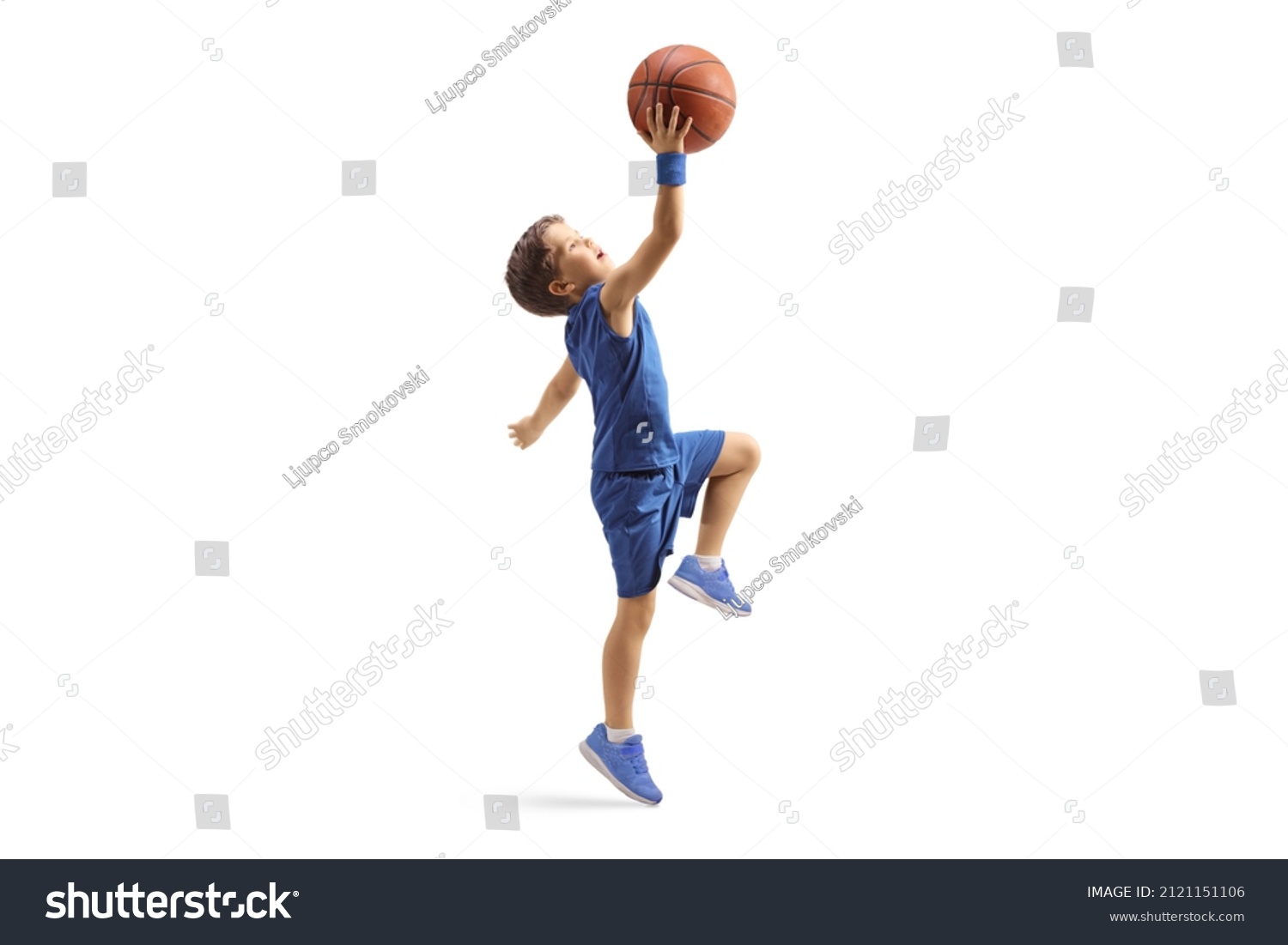 Full length profile shot of a boy in a blue jersey jumping with a basketball isolated on white background #2121151106