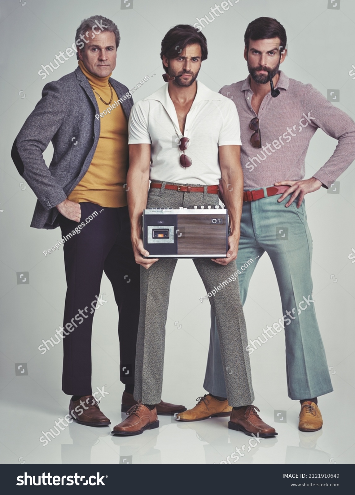 Ready to kick it retro style. A studio shot of three men clad in retro 70s wear holding a cassette player. #2121910649