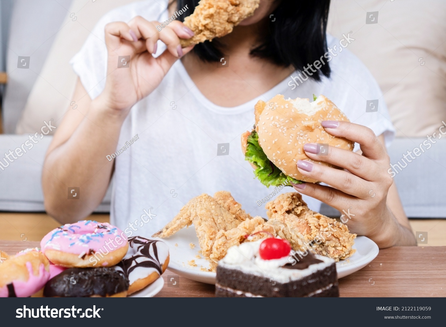 Binge eating disorder concept with woman eating fast food burger, fired chicken , donuts and desserts  #2122119059
