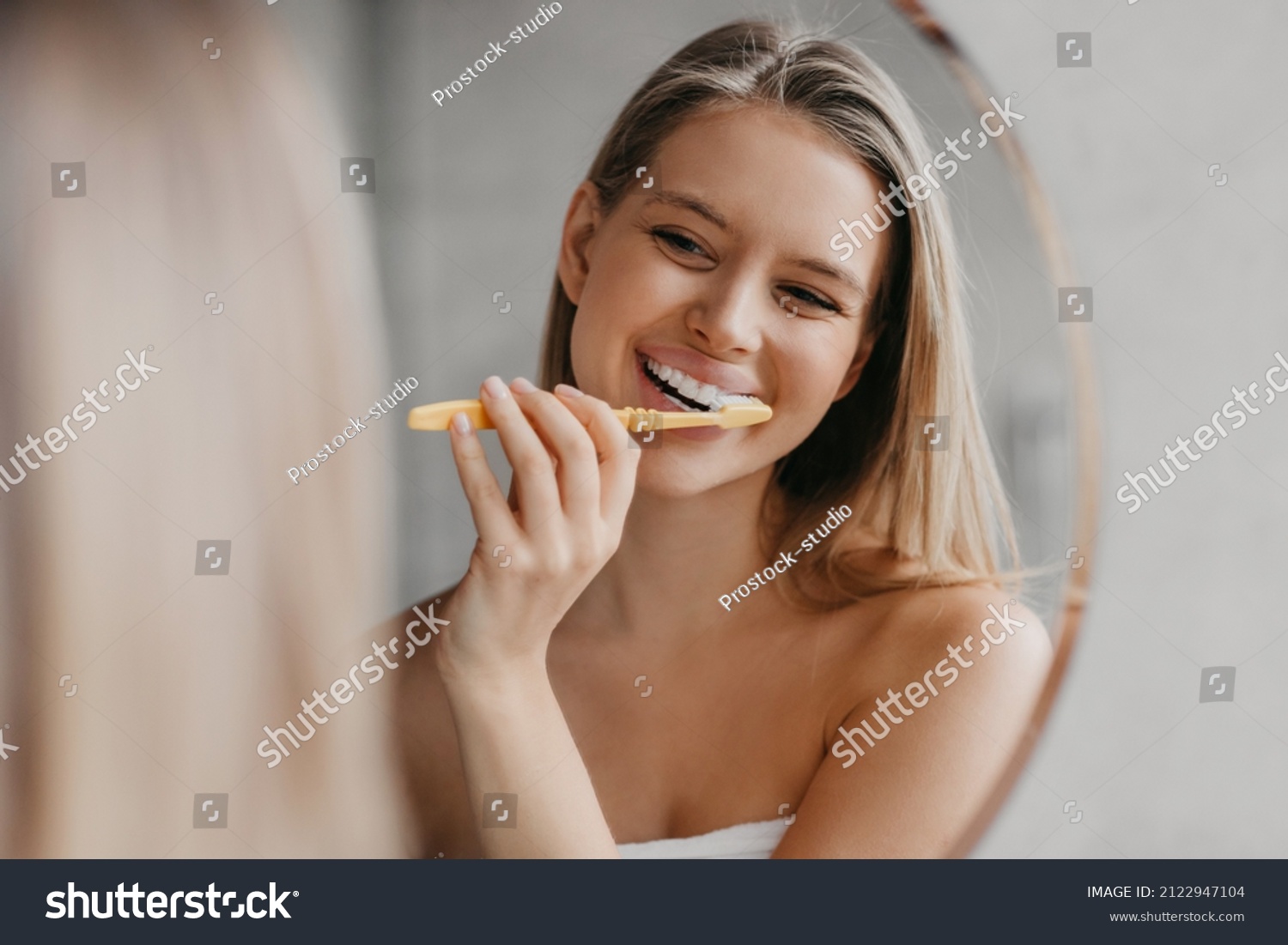Oral hygiene, healthy teeth and care. Young woman brushing teeth with toothbrush and looking in mirror in bathroom interior in the morning, closeup, empty space #2122947104