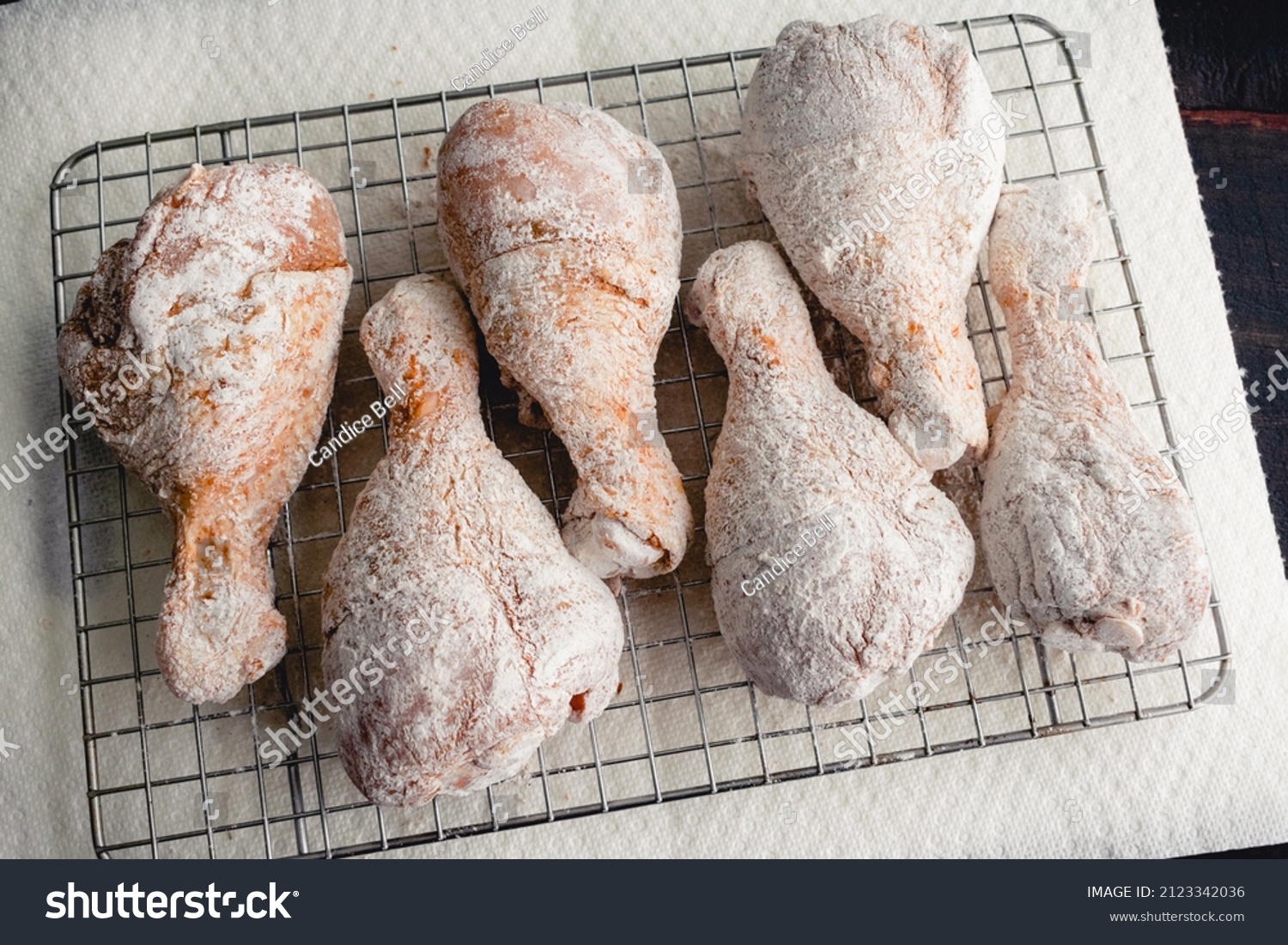 Raw Floured and Spiced Chicken Drumsticks on a Wire Rack: Floured uncooked chicken legs being prepped for frying #2123342036