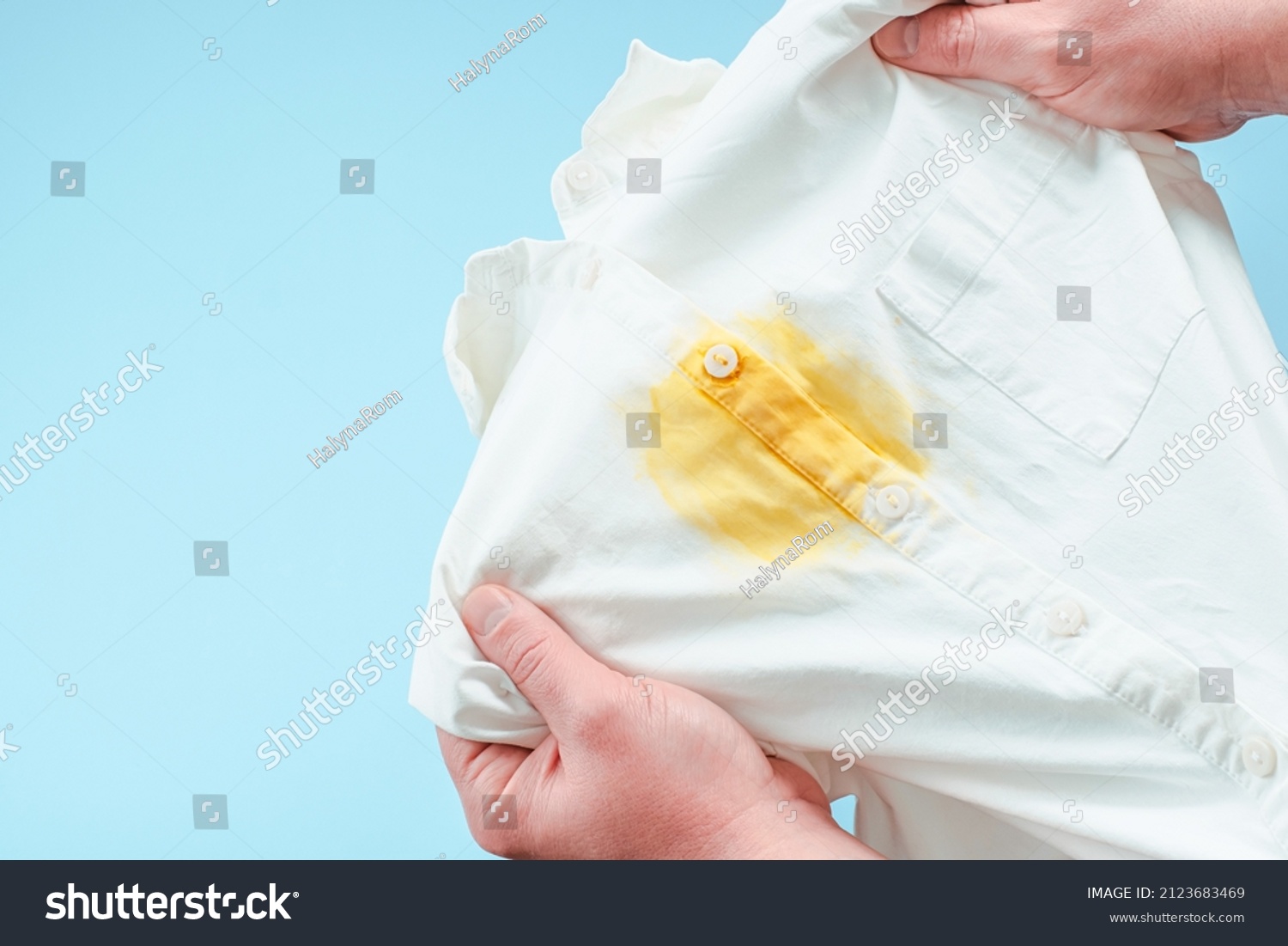 Dirty yellow stain on clothes. men's hands showing a white shirt. space for text. isolated. on blue background. top view. High quality photo #2123683469