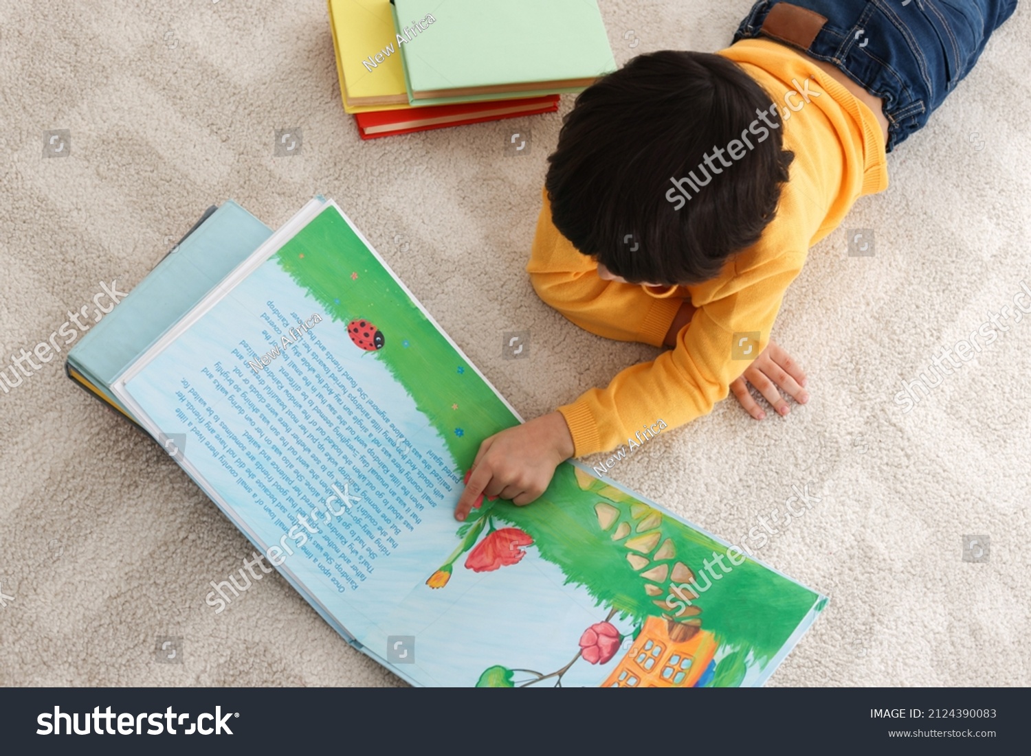 Cute little boy reading book on floor at home, above view #2124390083