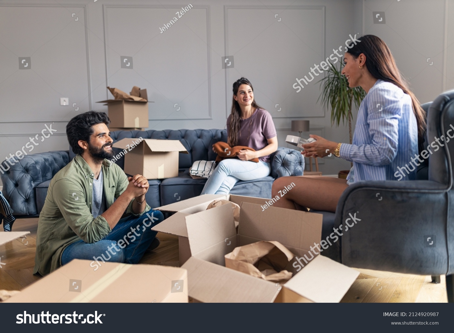 Friends sitting and talking in their new apartment while unpacking their things from cardboard box. #2124920987