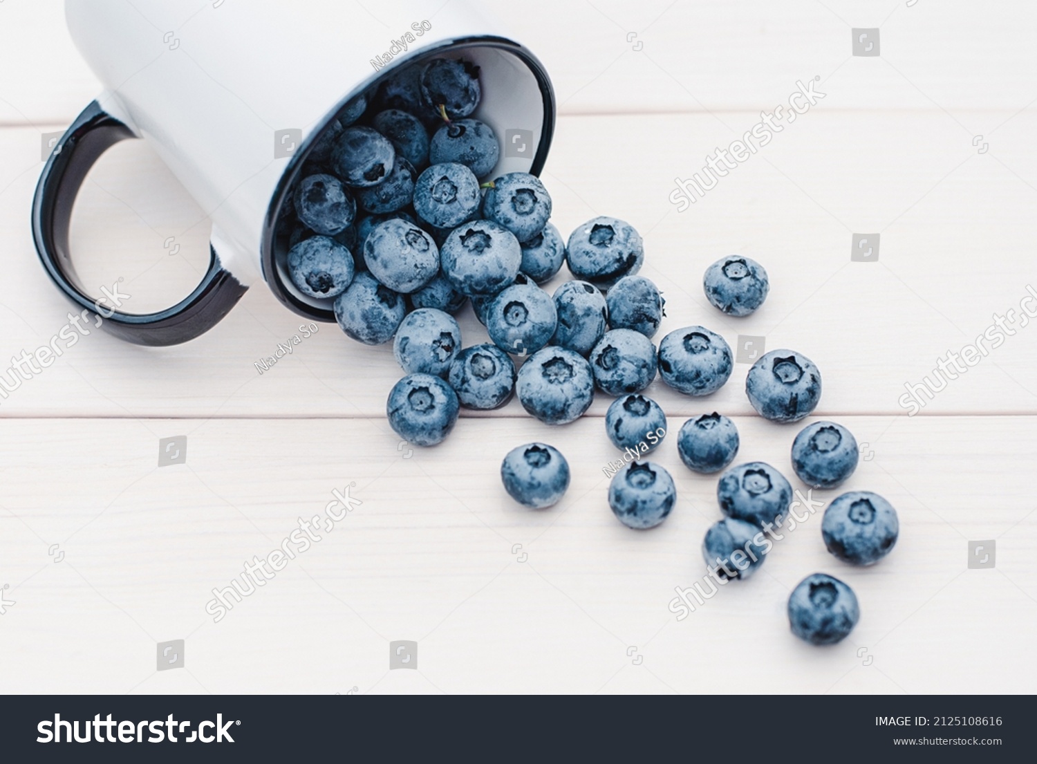 Blueberries slop out of a mug on white wooden table, blueberry fruit in a cup #2125108616