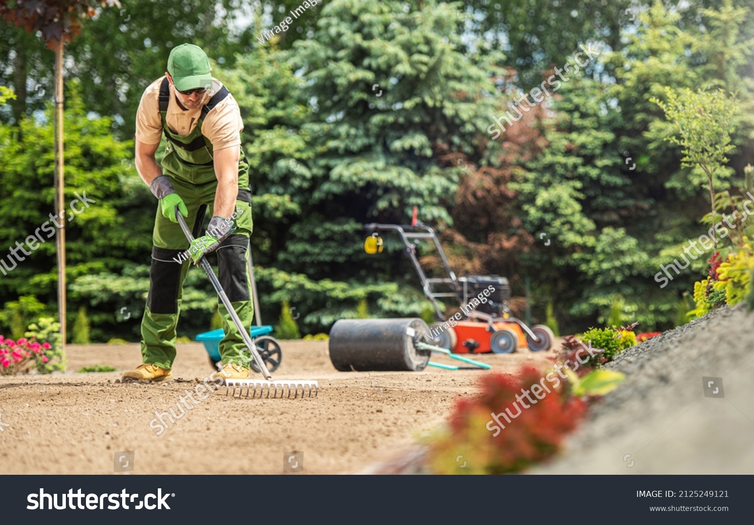 Caucasian Garden Specialist with Rake Preparing Soil For Natural Grass Turfs Installation. Landscaping Theme. #2125249121