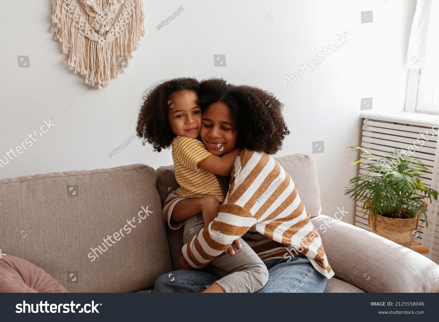 Younger and older sister spending time together at home. Two black girls of different age hugging and showing affection. Black female siblings having fun and bonding. Background, copy space, close up. #2125558046