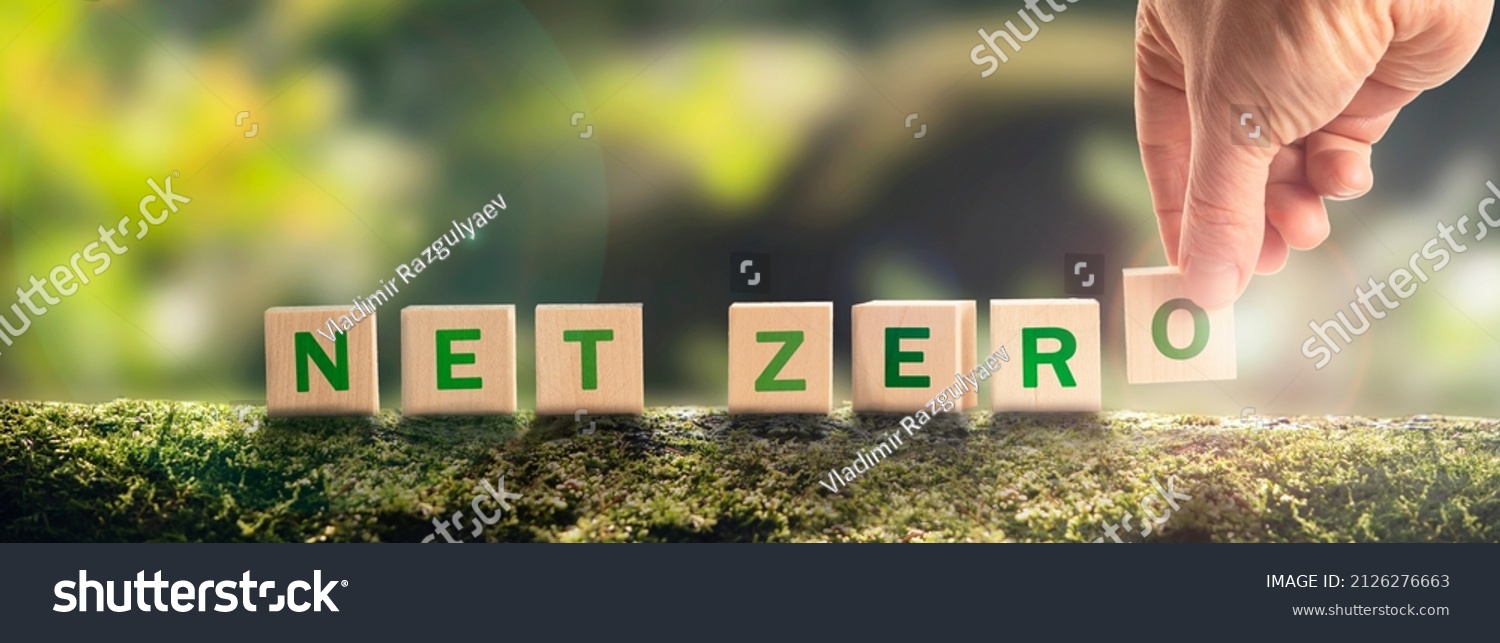 Net zero by 2050 Carbon neutral. Net zero greenhouse gas emissions target. Climate neutral long strategy. No toxic gases. Hand puts wooden cubes with netzero icon in green background panoramic #2126276663