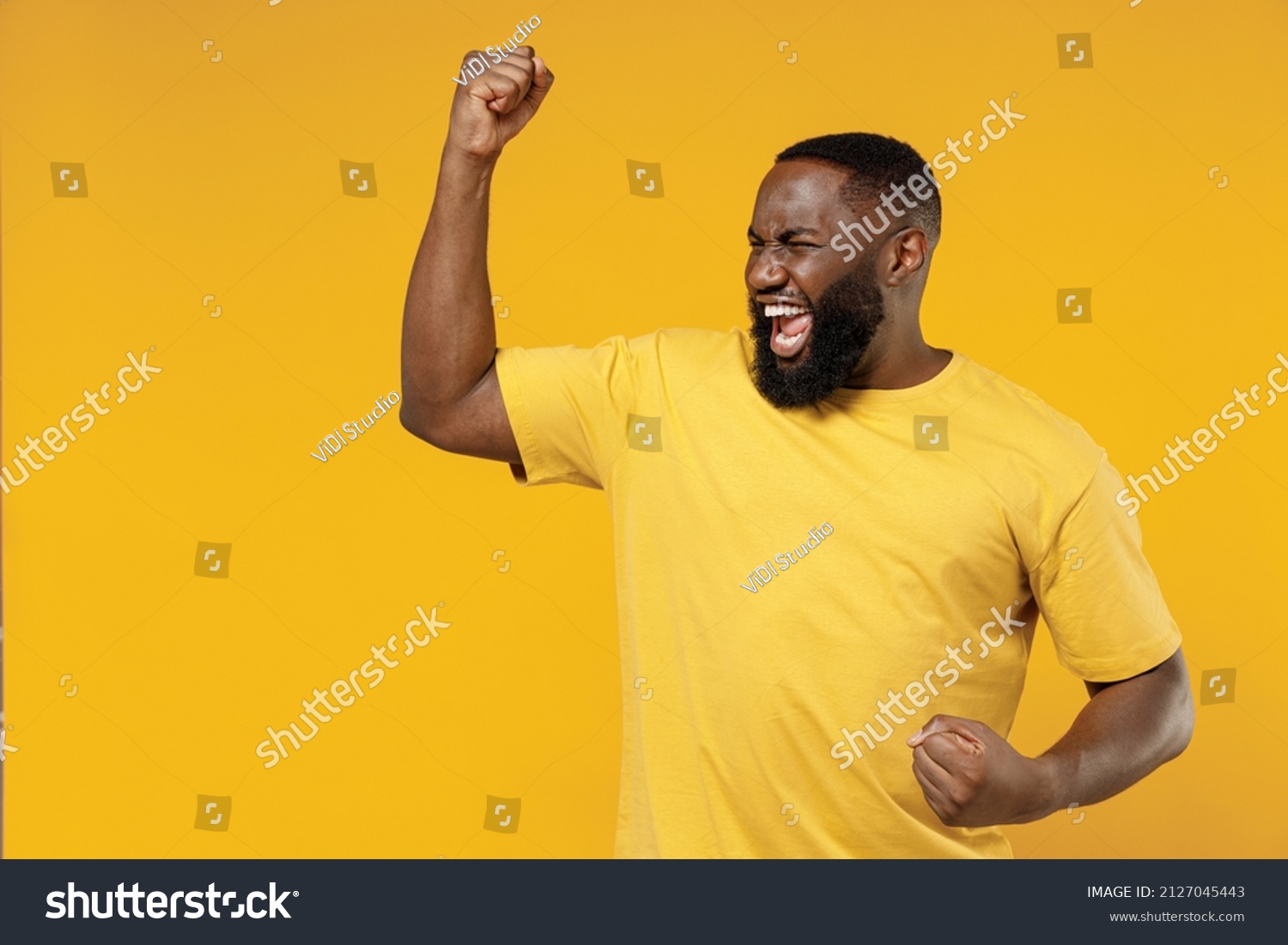 Young exultant happy black man 20s in bright casual t-shirt doing winner gesture celebrate clenching fists say yes isolated on plain yellow color background studio portrait. People lifestyle concept #2127045443