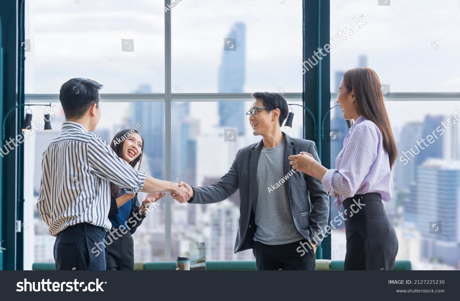 Asian business team leader congratulate his teammate employee for the outstanding achievement team performance by shaking hand in the modern office workplace with skyscraper view #2127225230