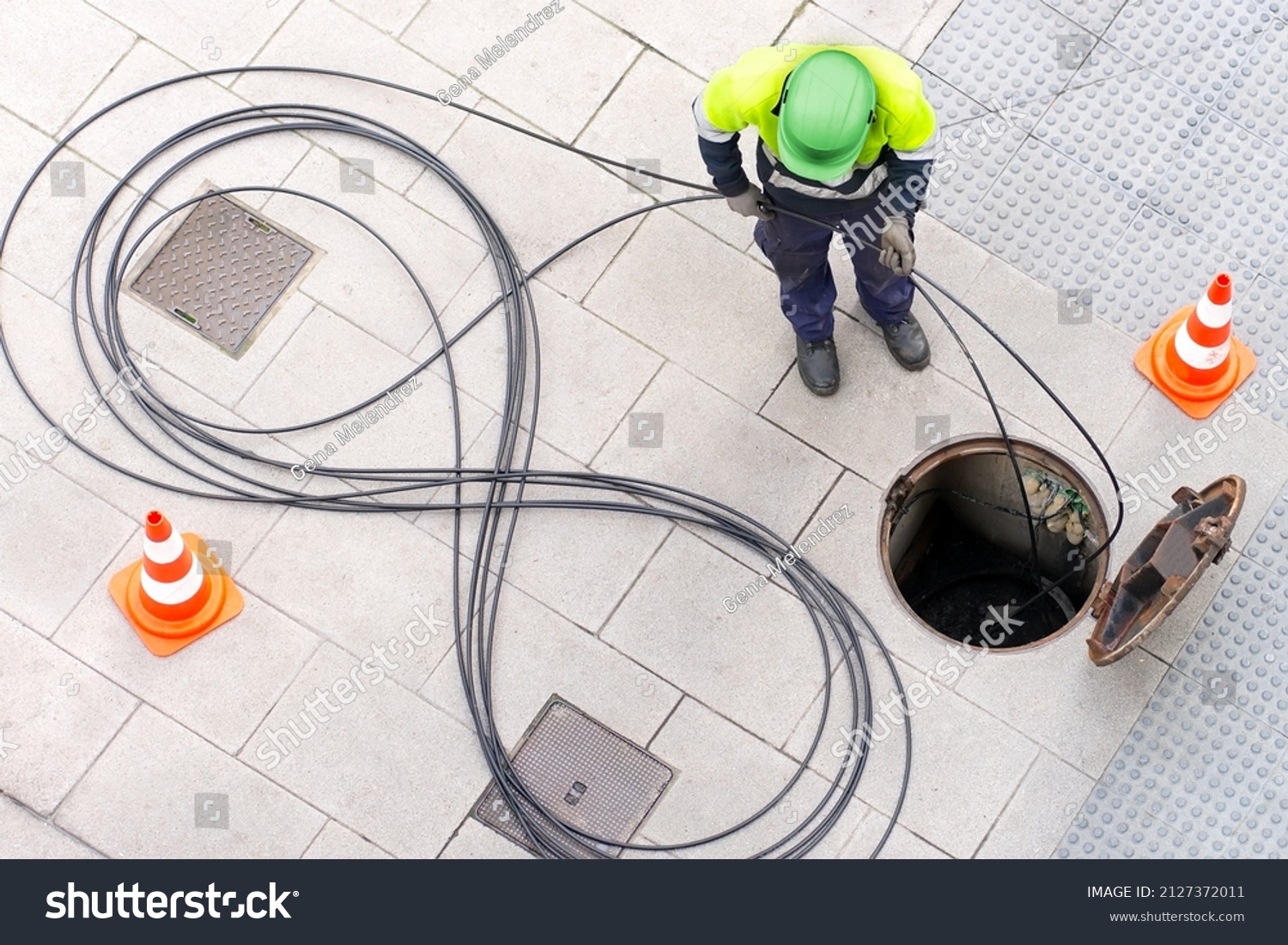electrician worker install optical fiber cable for internet and telephone underground lines  in city street #2127372011