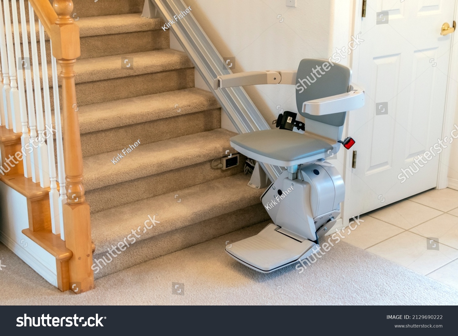 An electric, motorized chair lift for persons with disabilities on a carpeted staircase in a residential home. #2129690222