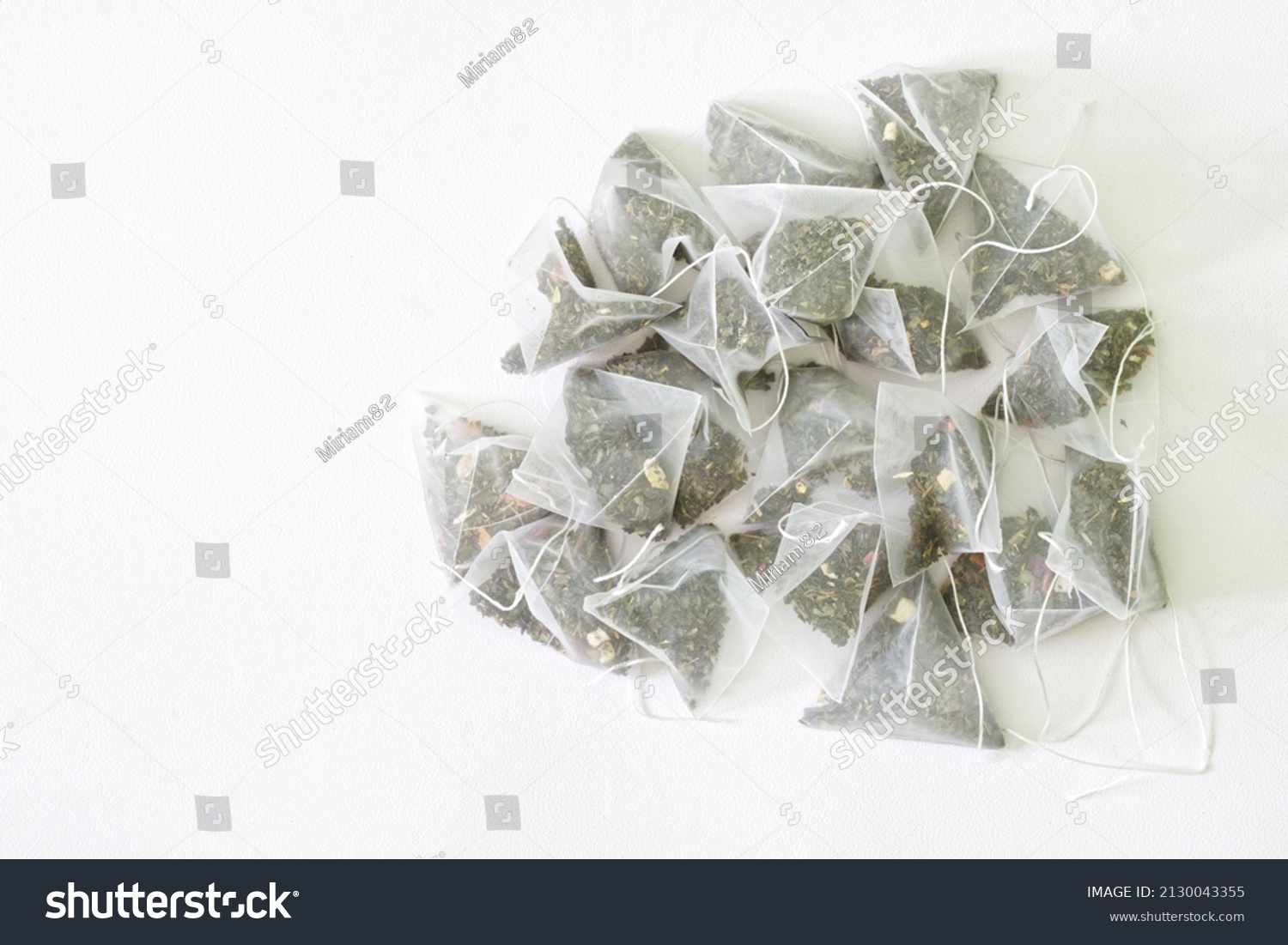 Bunch of tea bags-pyramids with green tea with the addition of fragrant fruits. Textured white background. Copy space for an inscription. Daylight #2130043355