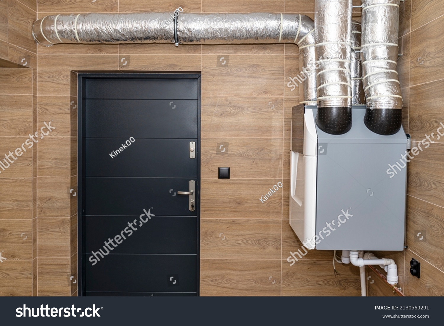 Home mechanical ventilation with heat recovery hanging on the wall in a modern gas boiler room with brown ceramic tiles imitating wood. #2130569291