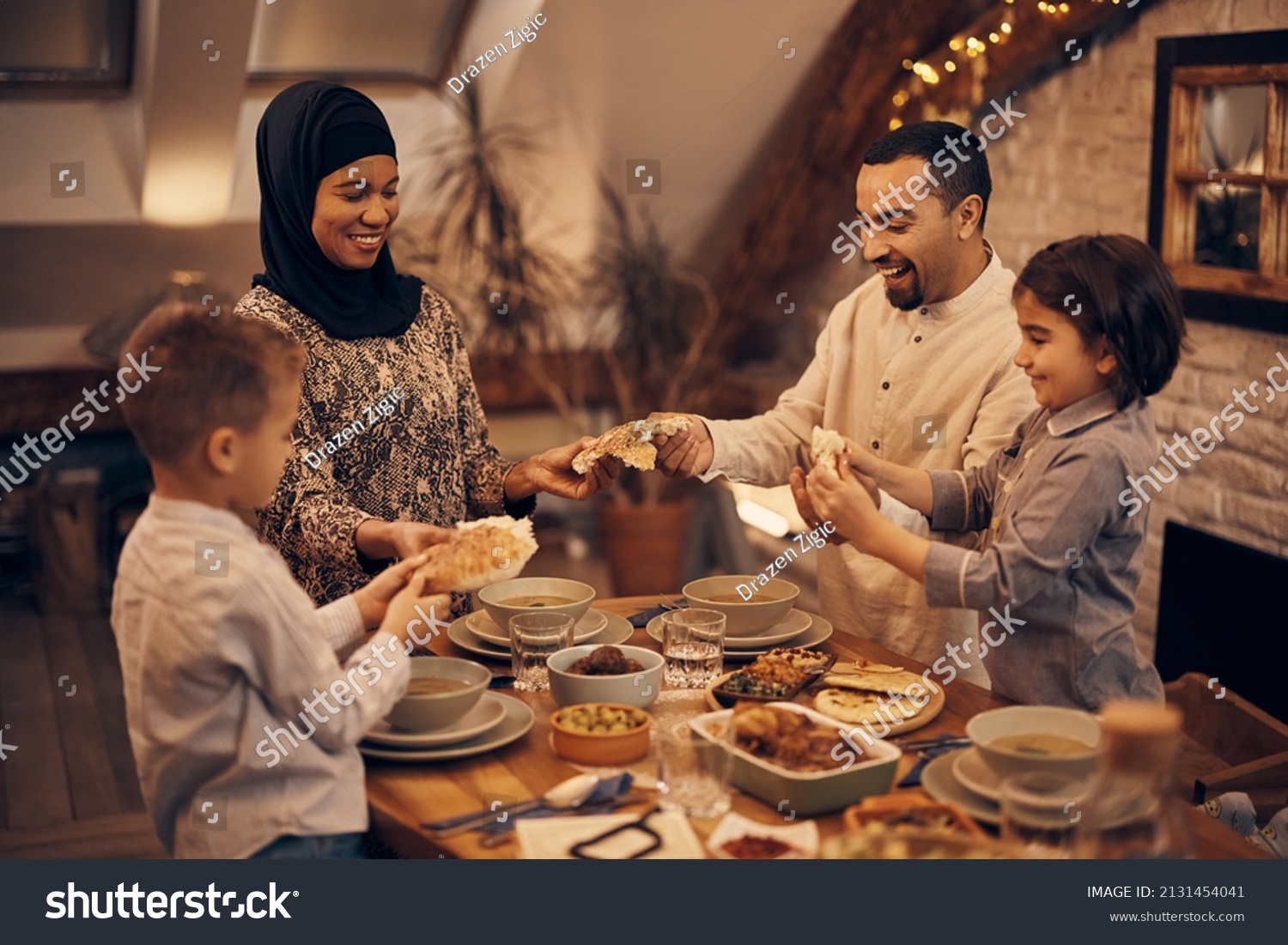 Happy Muslim parents and their kids sharing pita bread while eating dinner on Ramadan at home.  #2131454041