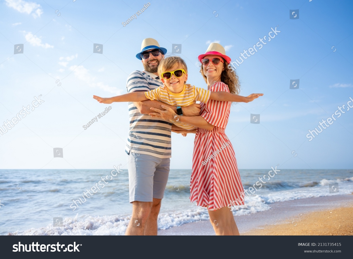 Happy family having fun on the beach. Mother and father holding son against blue sea and sky background. Summer vacation concept #2131735415