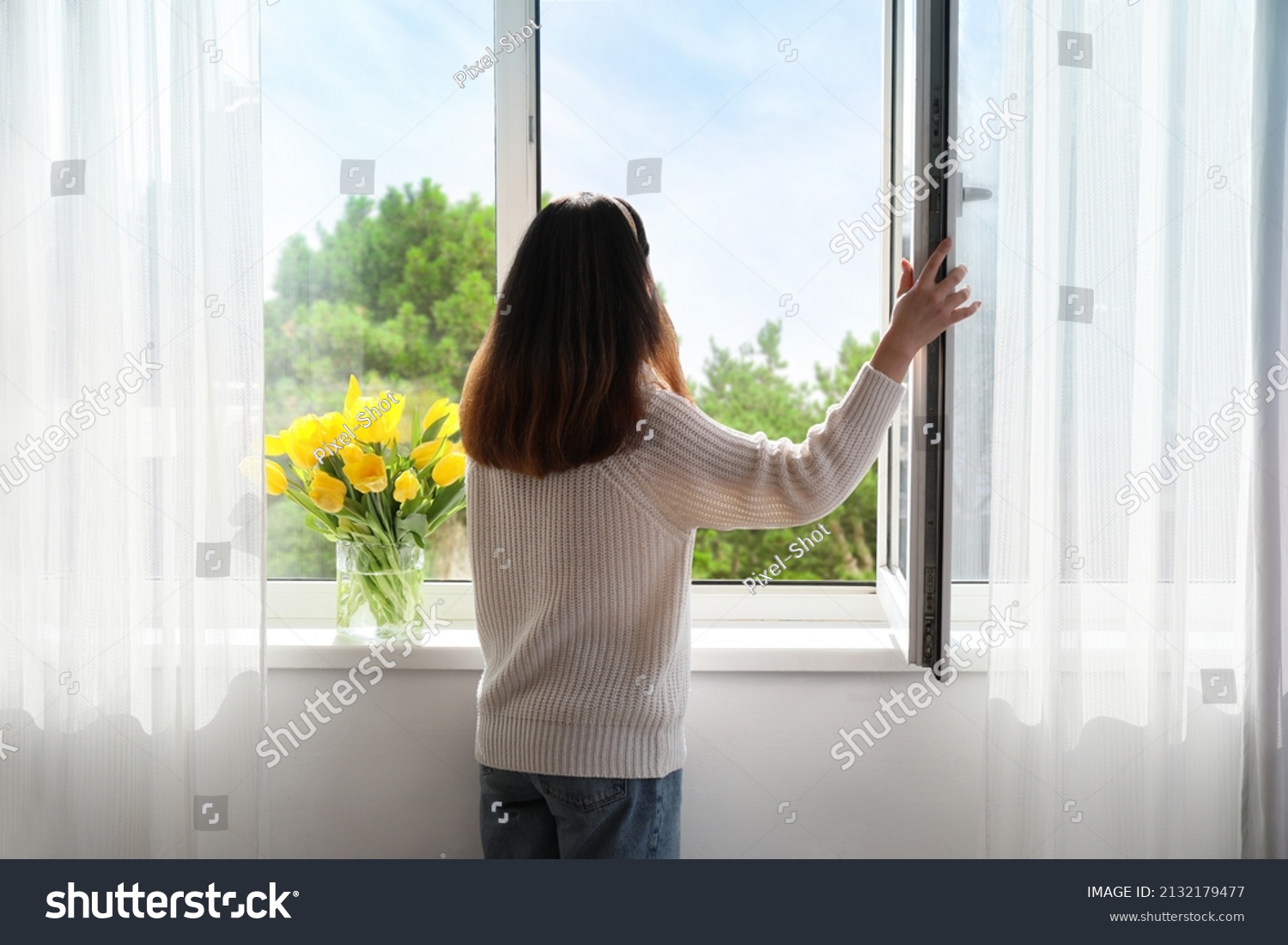 Pretty young Asian woman opening window at home on sunny day, back view #2132179477