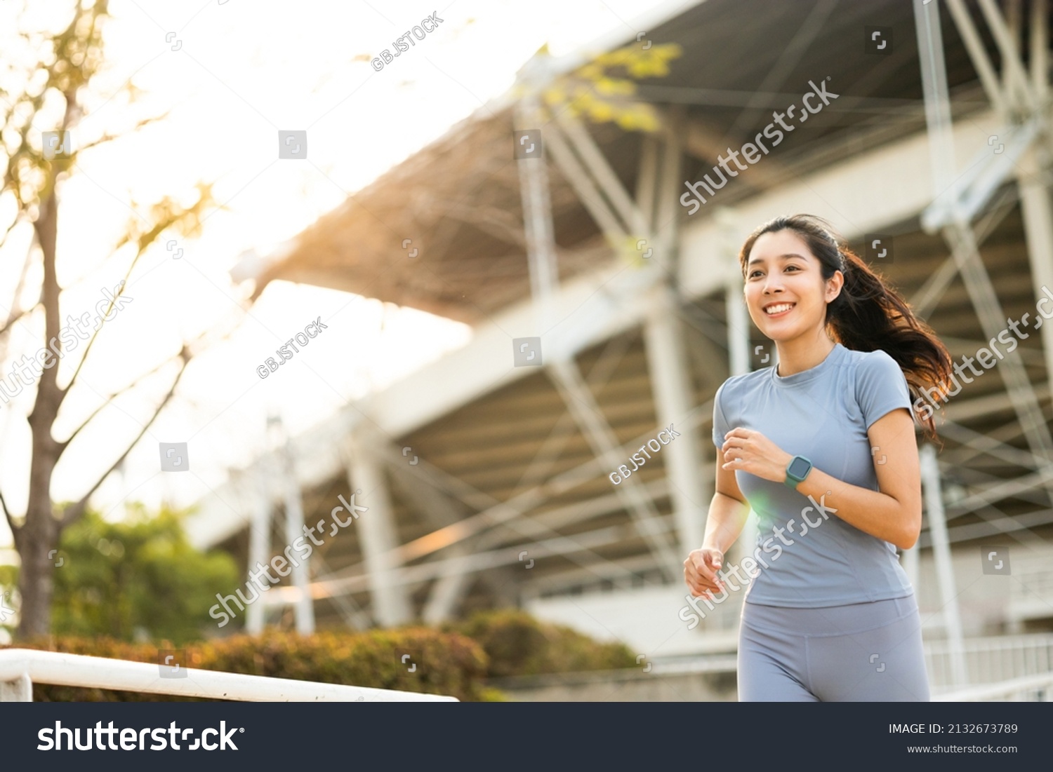 Attractive beautiful woman wearing sportswear running at sport stadium. Fit woman jogging outdoor. Workout exercise in the morning. Healthy and active lifestyle concept. #2132673789
