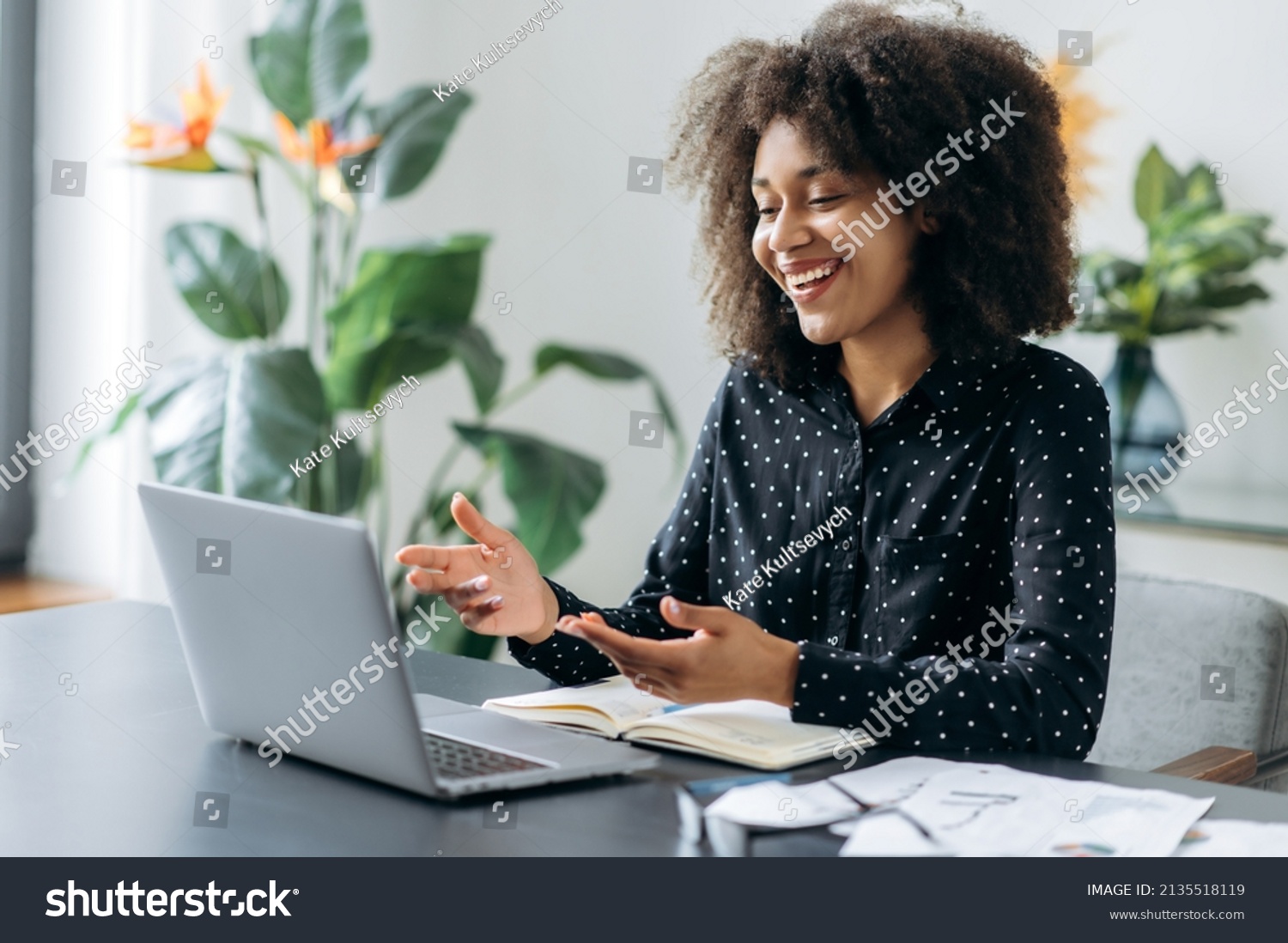 Successful positive young adult woman african woman freelancer, manager, CEO, sitting in office at laptop, talking on video call with client or employees, discussing business strategy, gesturing,smile #2135518119